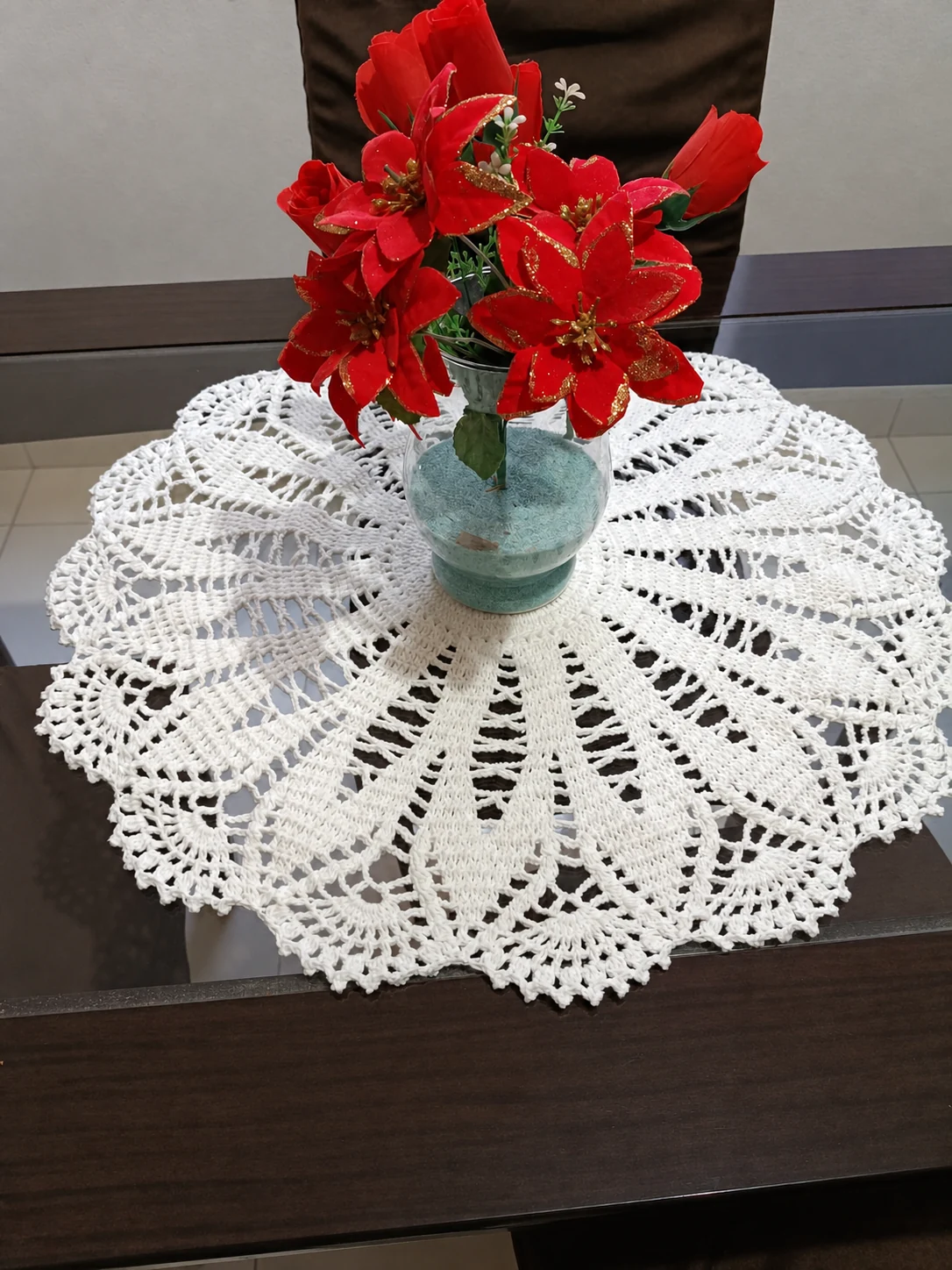 Toalha redonda de crochê branco com um vaso de flores vermelhas